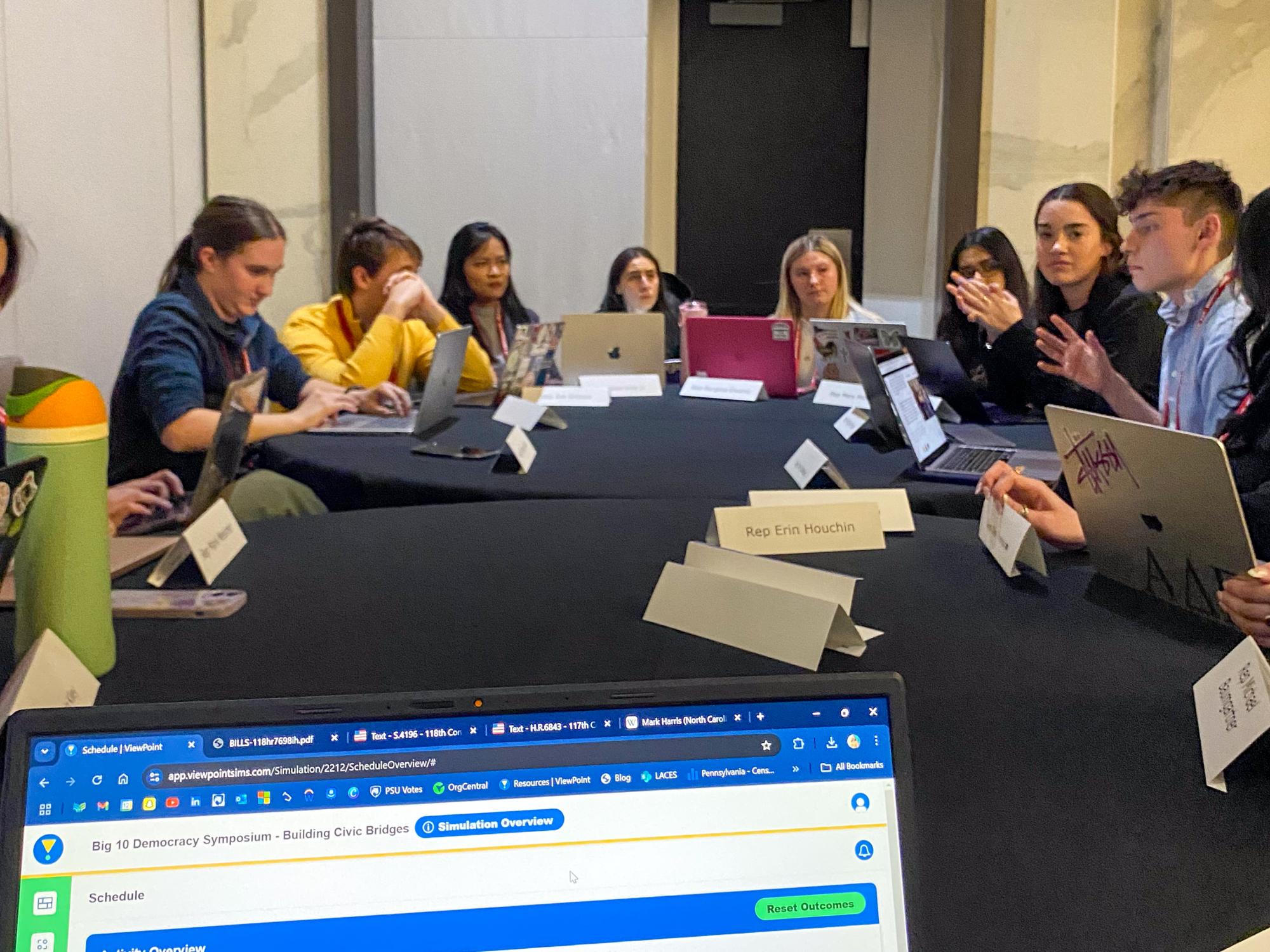 Students sit around a table with laptops during a policy simulation.