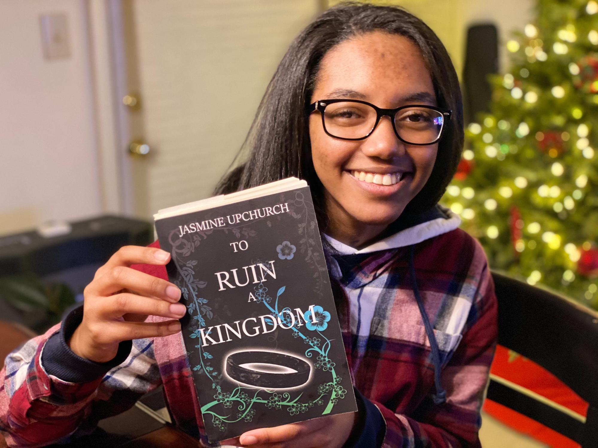 Jasmine Upchurch holding a copy of her first published novel titled “To Ruin a Kingdom.”