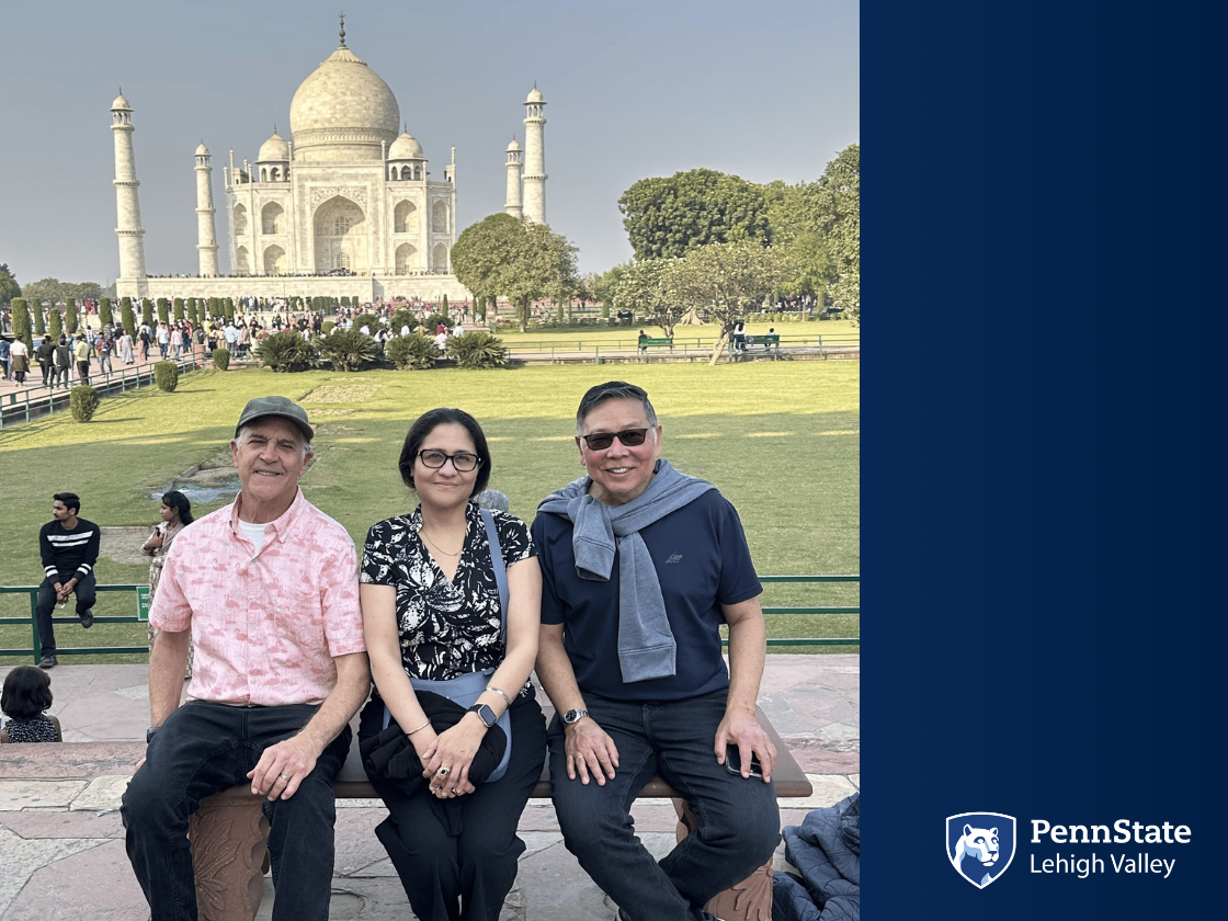 two men and a woman sit on a bench and smile in front of the Taj Mahal in India