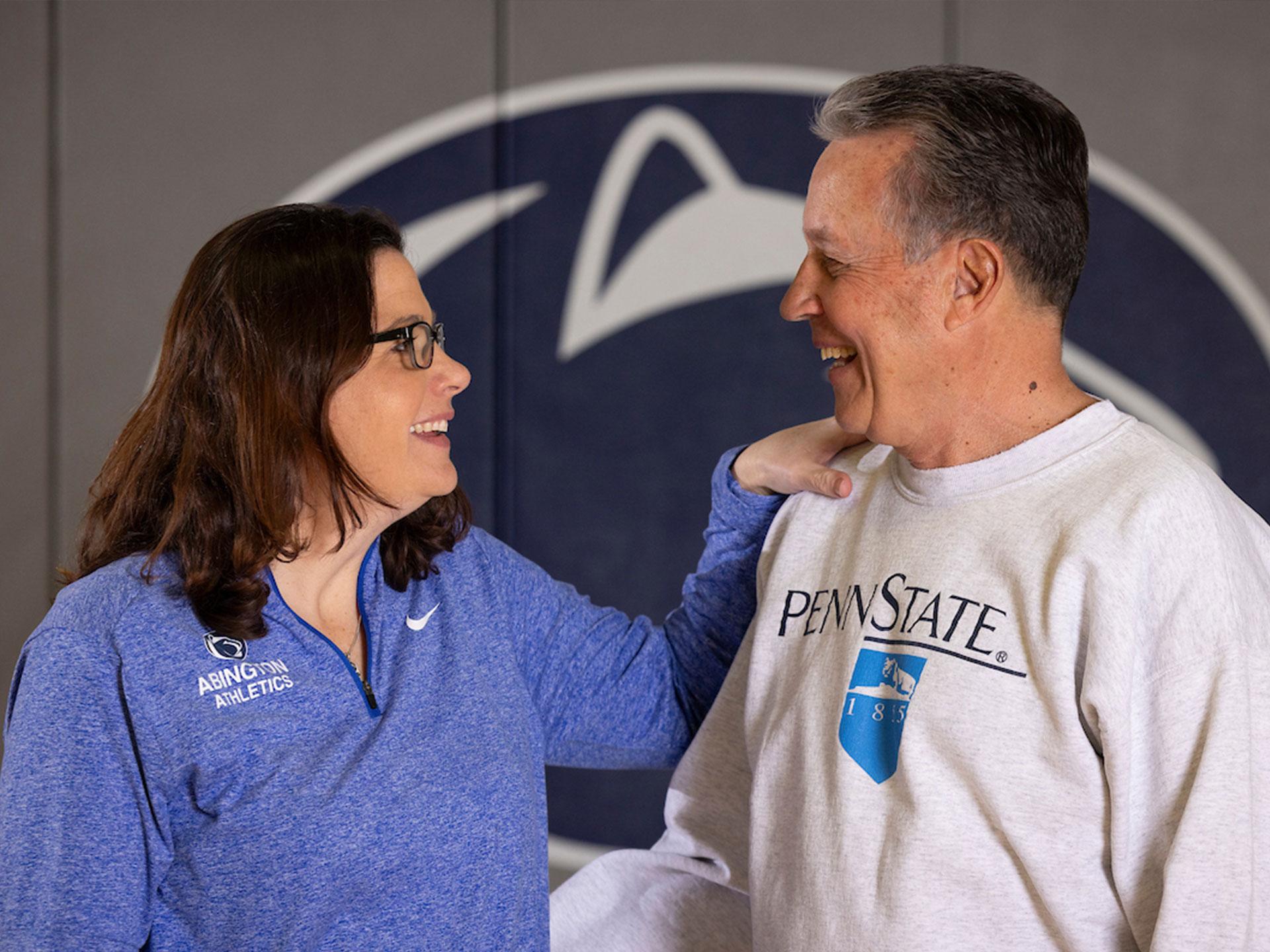 Woman and man talking in front of Penn State athletics logo