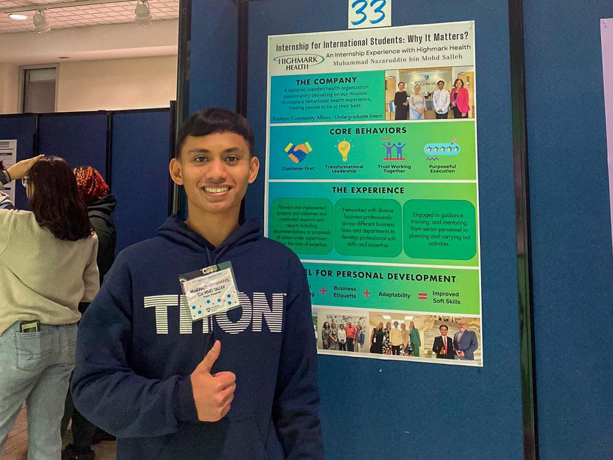 Muhammad Nazaruddin bin Mohd Salleh smiles and gives a thumbs up while standing in front of a poster about his internship with Highmark Health at the 2024 Student Engagement EXPO.