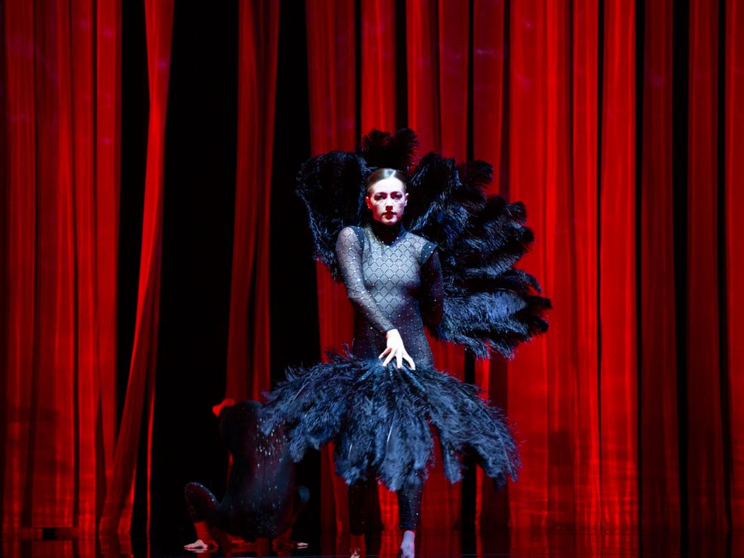A woman wears a leotard adorned with large feathers.
