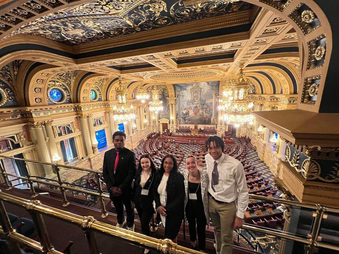 a group of students stands on a balcony looking over large room in state capitol building