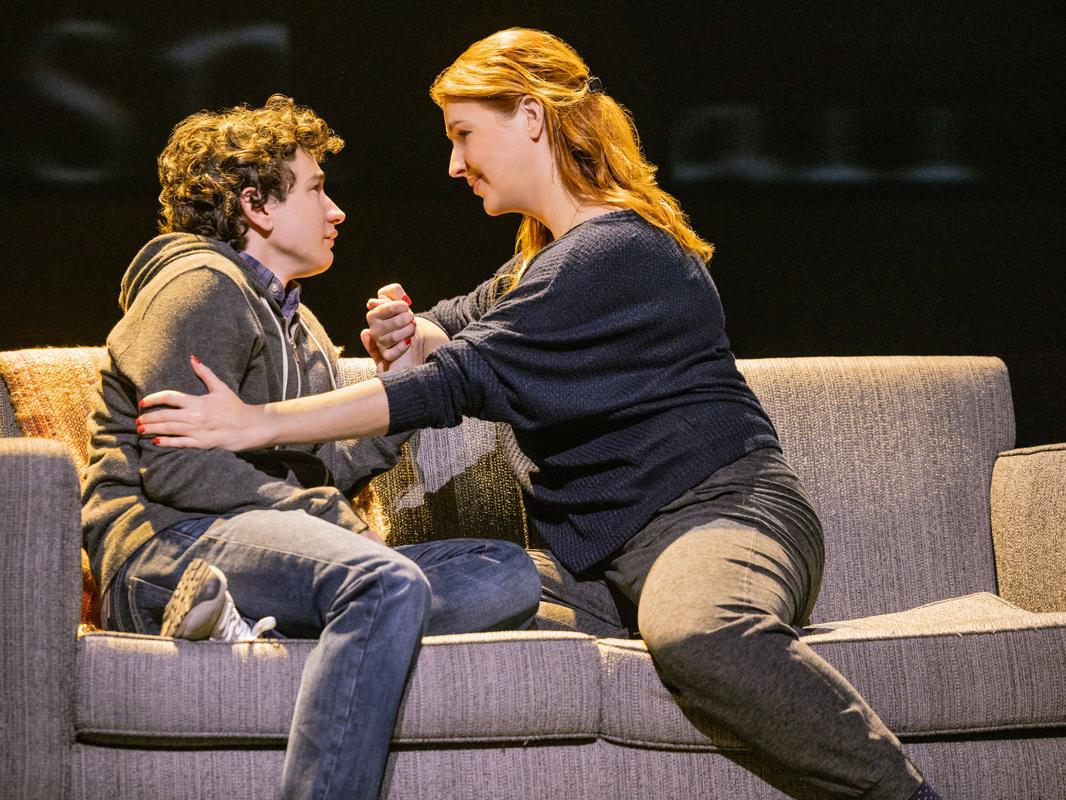 A middle-aged woman consoles a crying teenager on a couch.