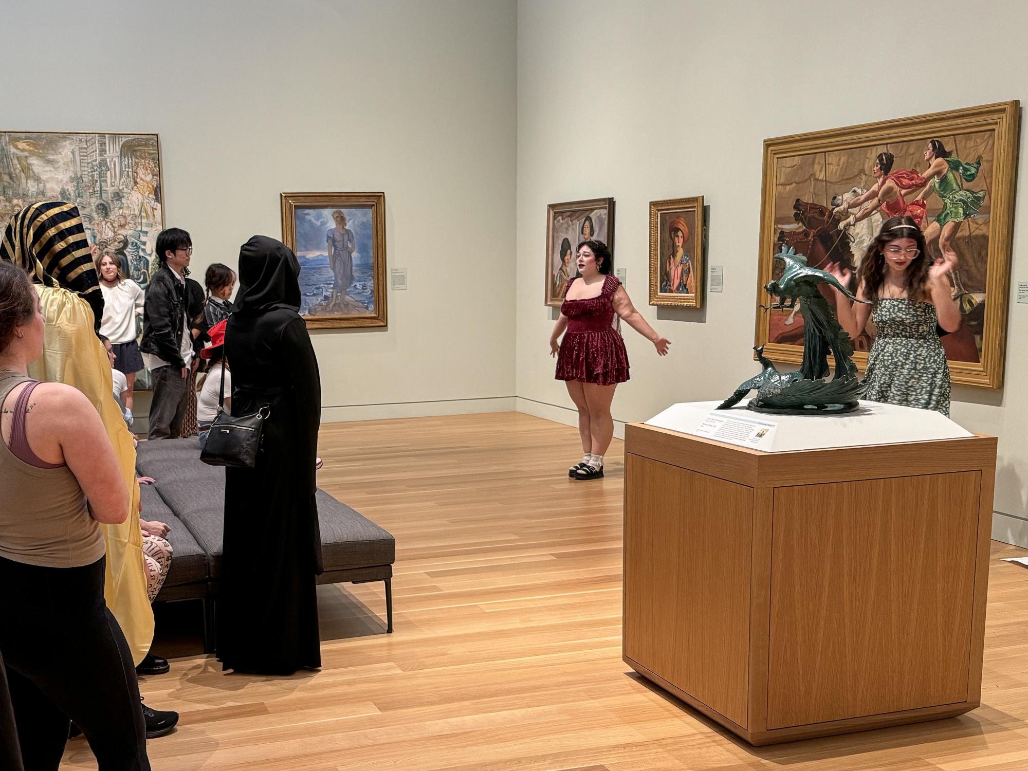 Amanda Demuth (center) and another intern (right) stand in front of paintings while presenting to a group of people at the Palmer Museum of Art.