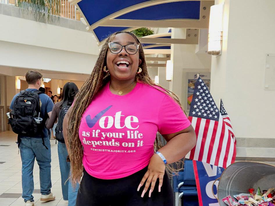 Noa Diggs stands in a bright pink shirt while advocating for gender equality in the HUB-Robeson Center as a campus organizer for the Feminist Majority Foundation.
