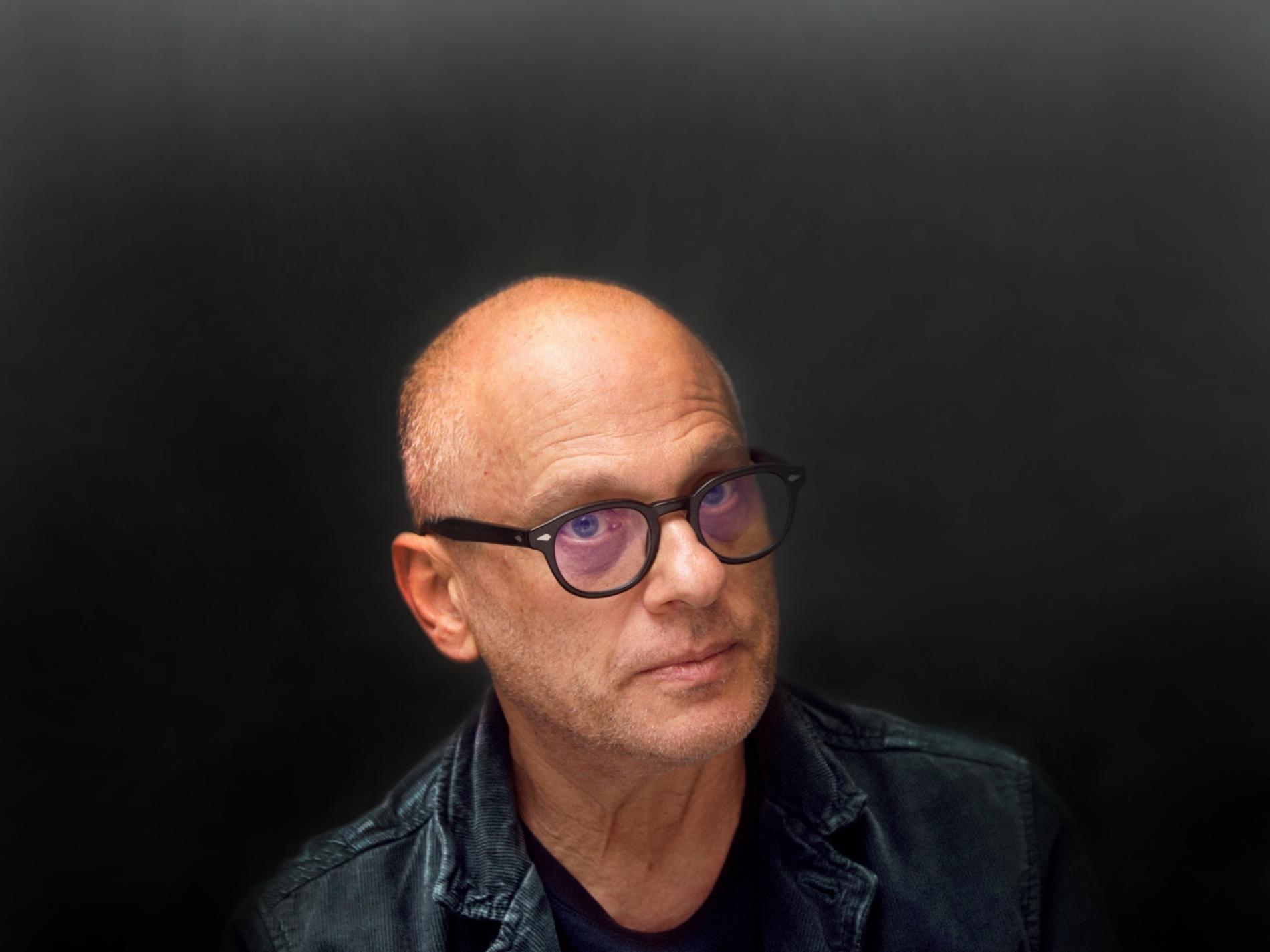 A bald white man wearing glasses gives a serious look.	
