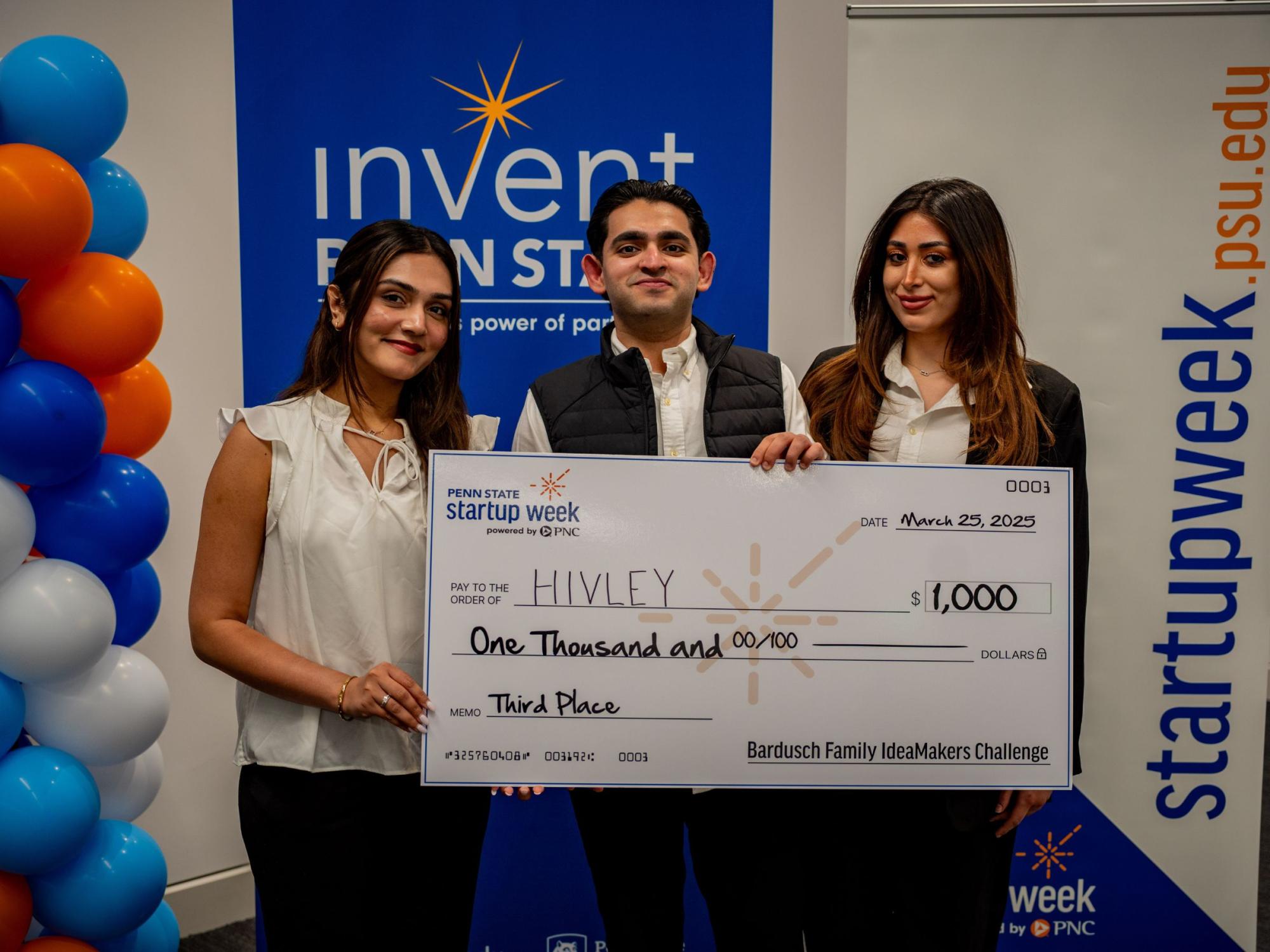three smiling people display giant check
