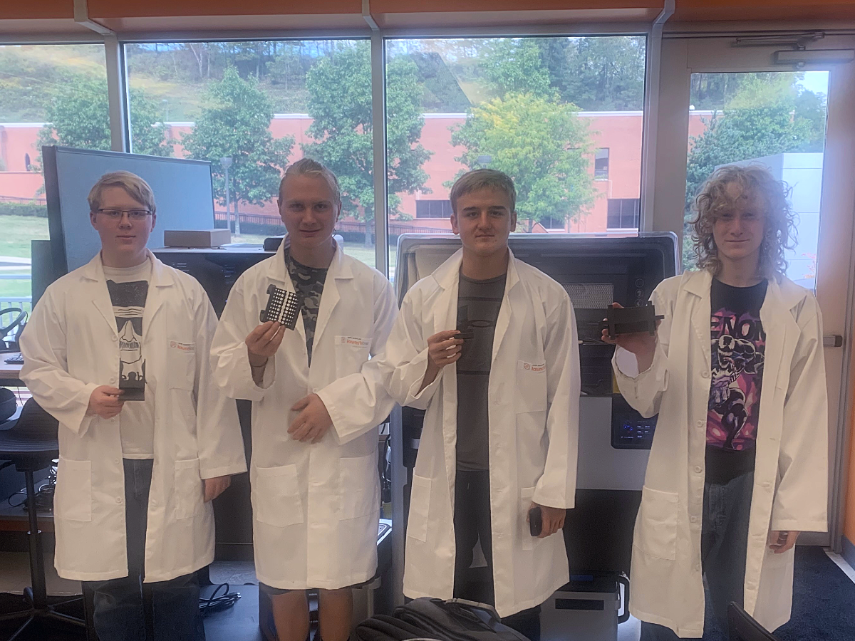 Four students in lab coats holding 3-D printed items