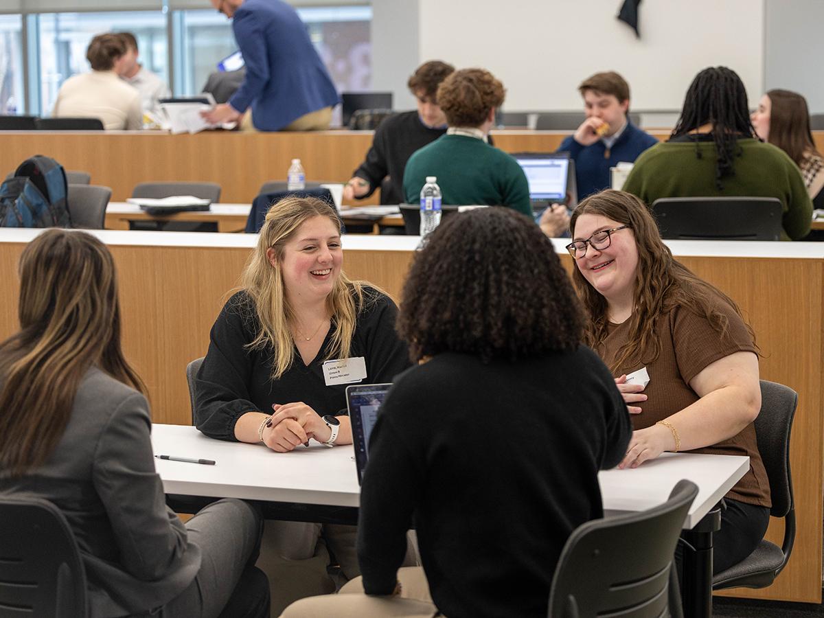 Four students sitting around a desk and laughing during Policy Simulation Competition