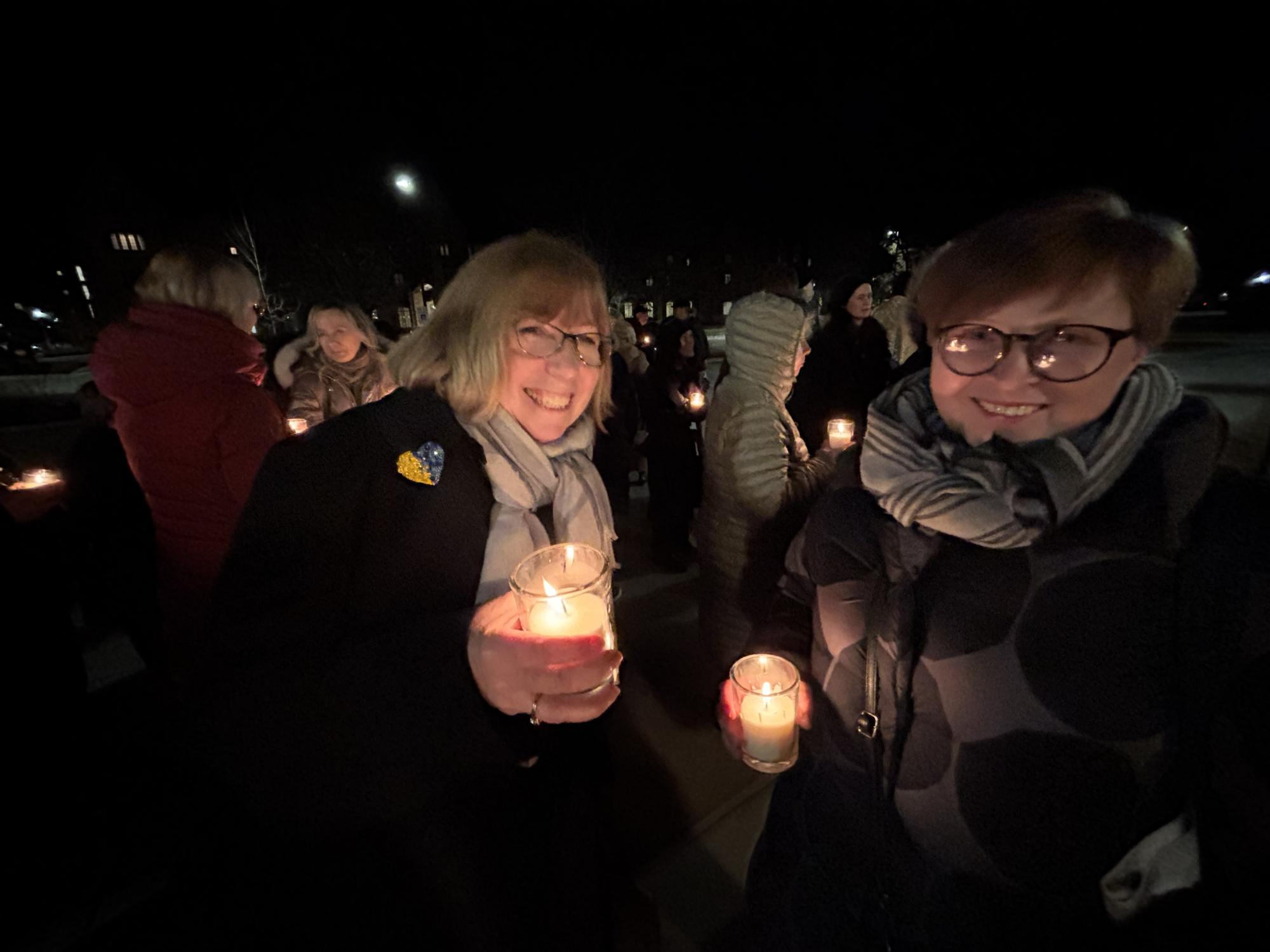 Two women hold candles at an outdoor event held at night 