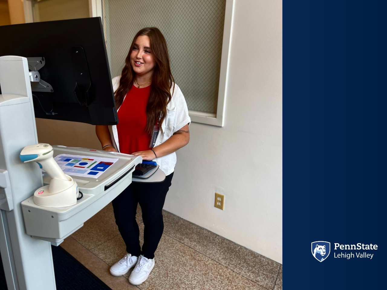 a female college student stands at a computer inside a hospital room