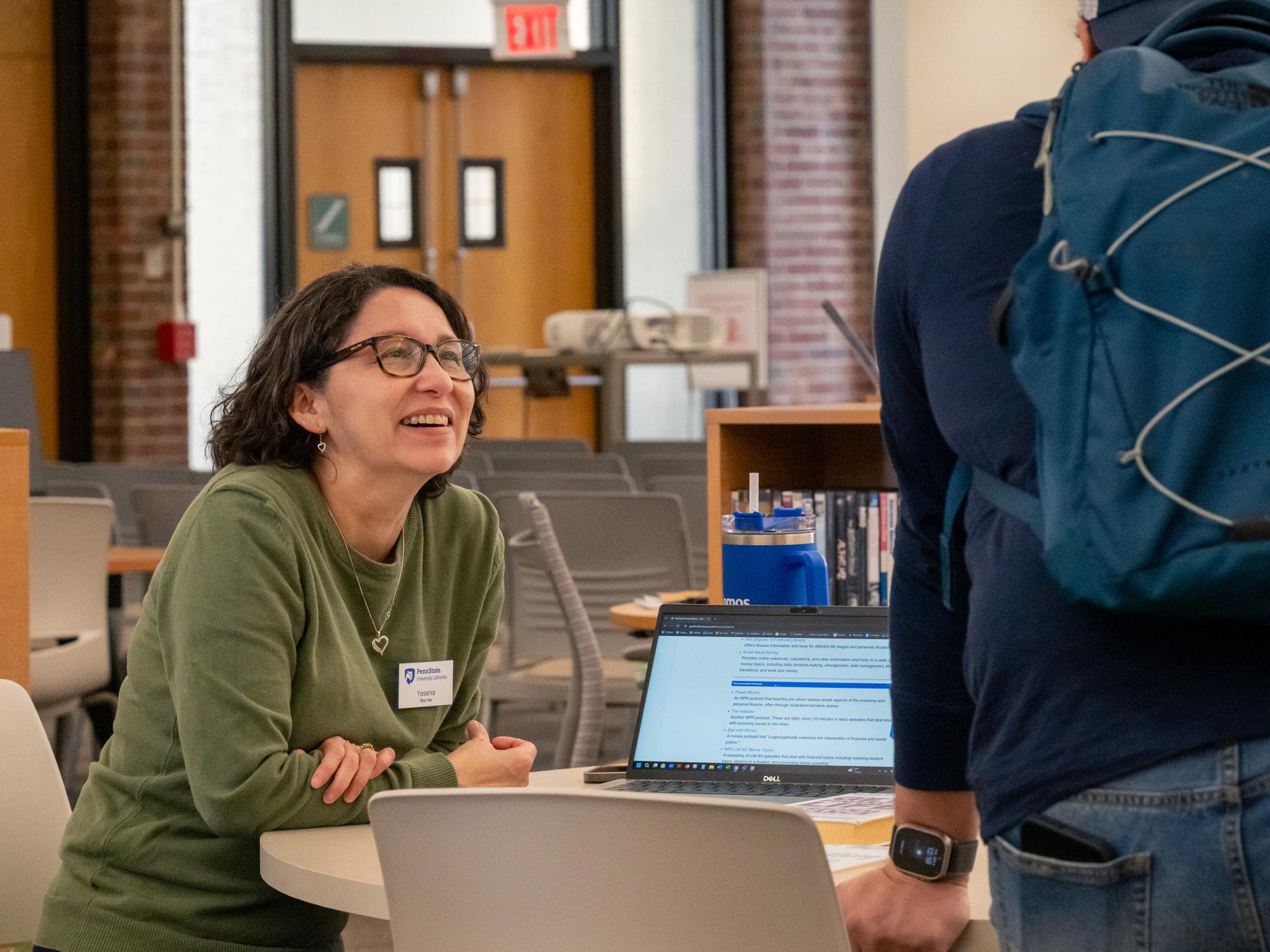 Yesenia, Library Operations Supervisor at Penn State New Kensington's Blissell Library, chats with a student near an information desk.
