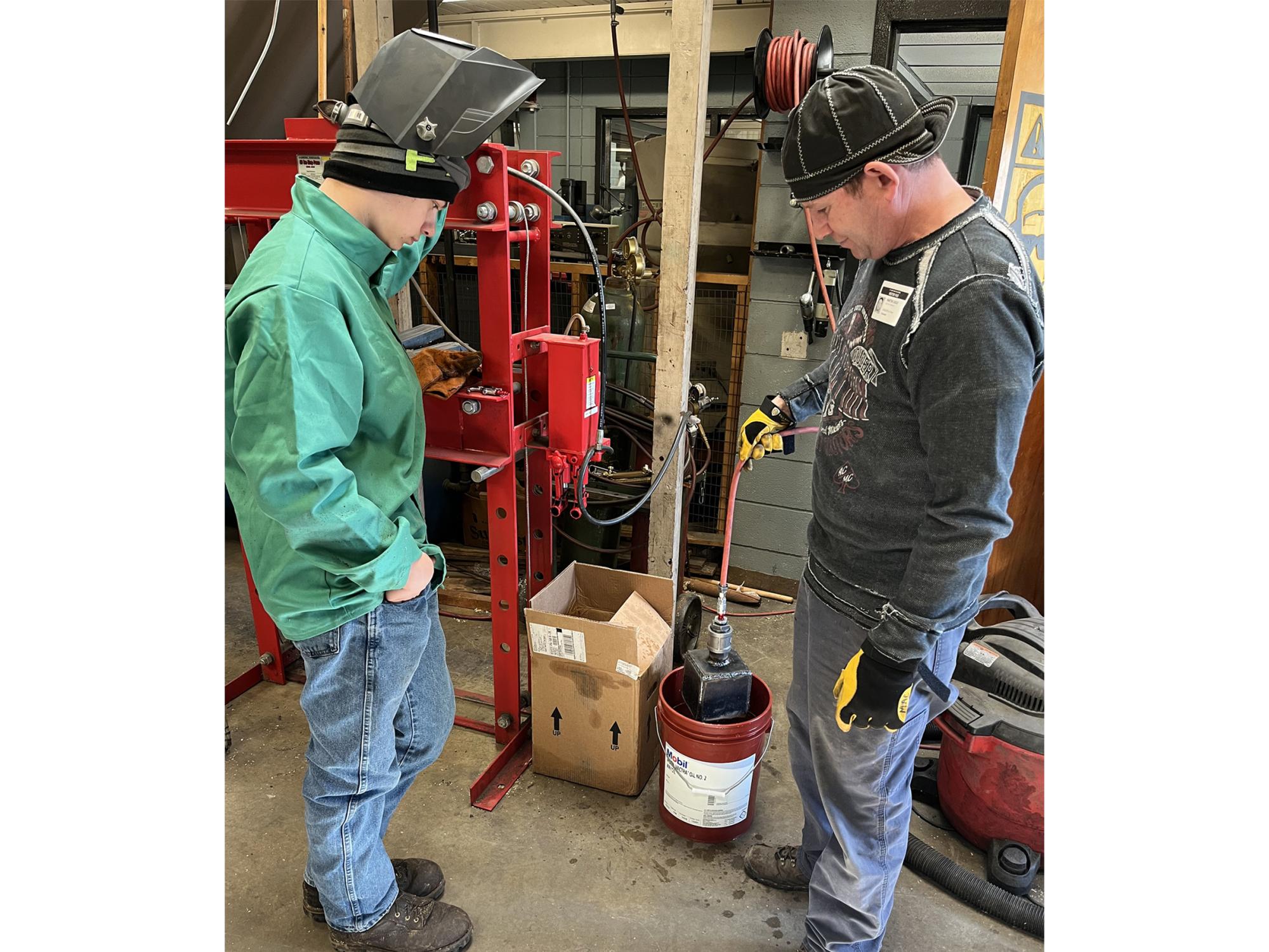 Dutch Manufacturing student Sam Rettger, left, and instructor Martin Casilio, test whether Rettger’s cube project is air-tight by submerging the project in water while connected to compressed air.
