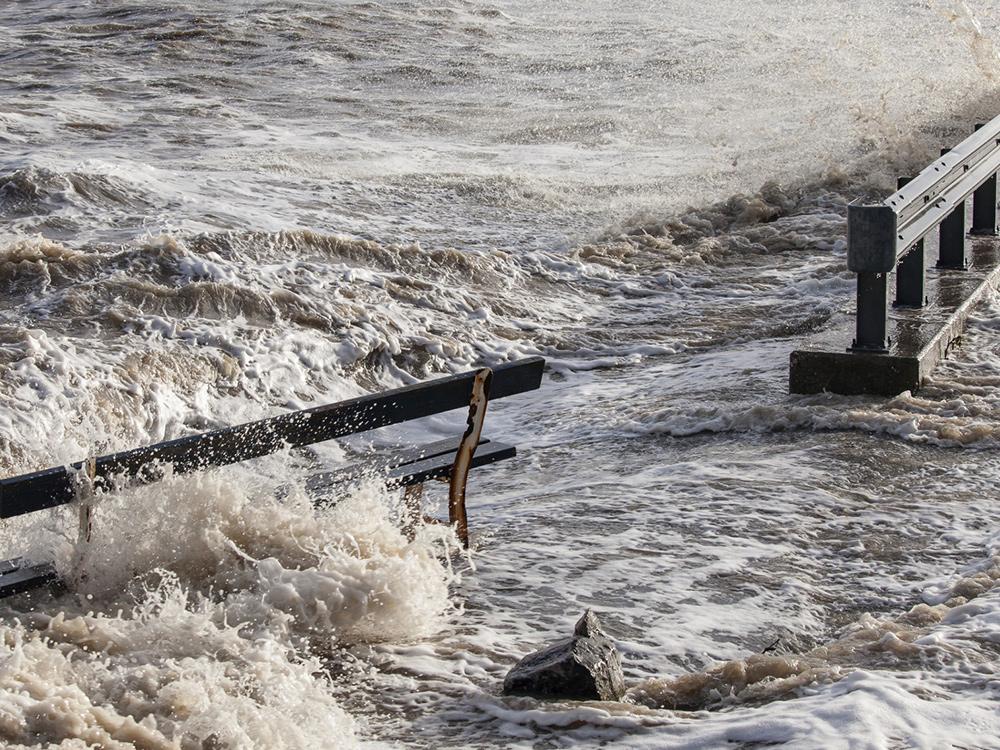 tides extend onto concrete with water splashing over bench