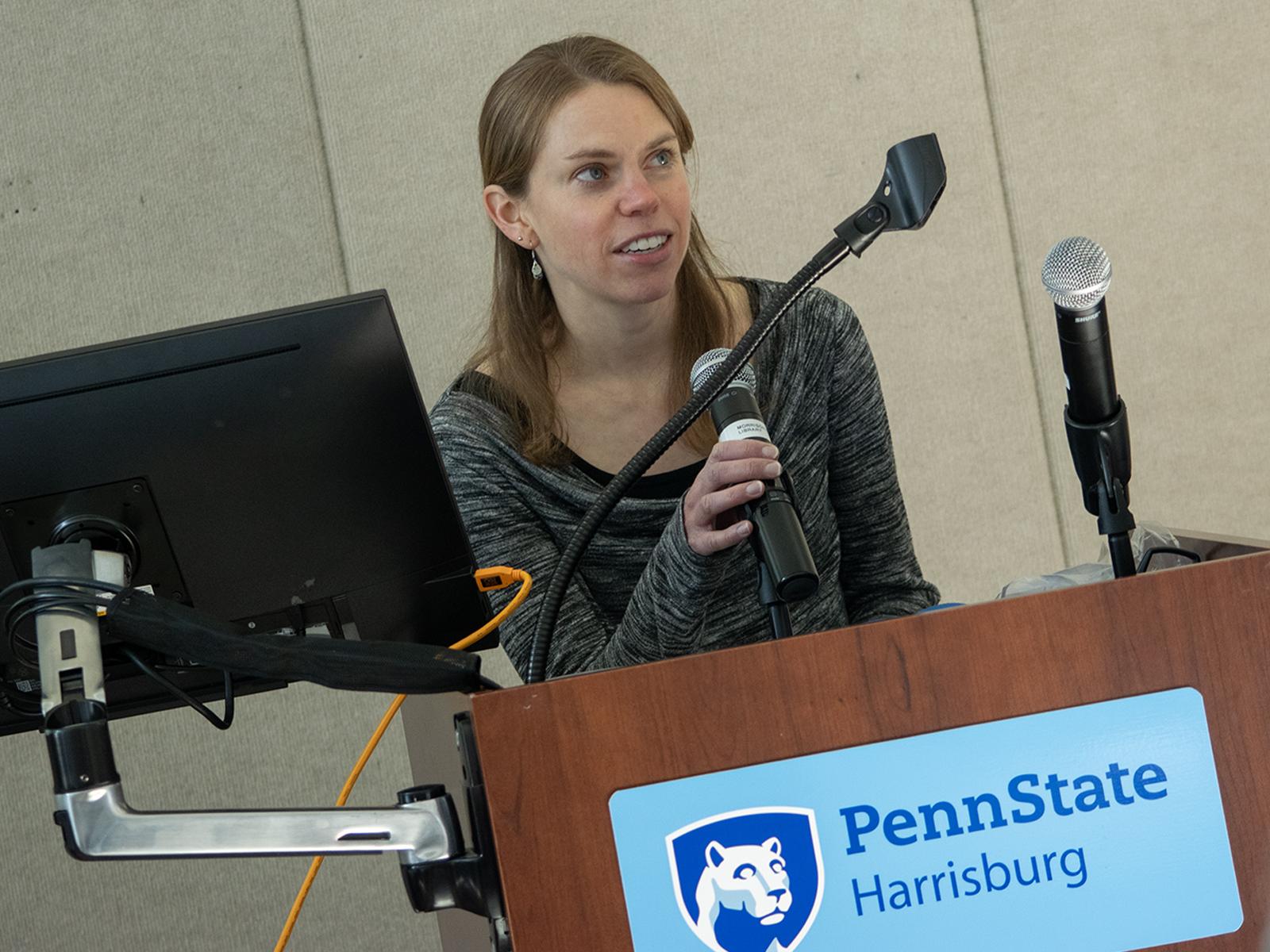 A woman speaks from behind a lectern, which has a Penn State Harrisburg logo on it