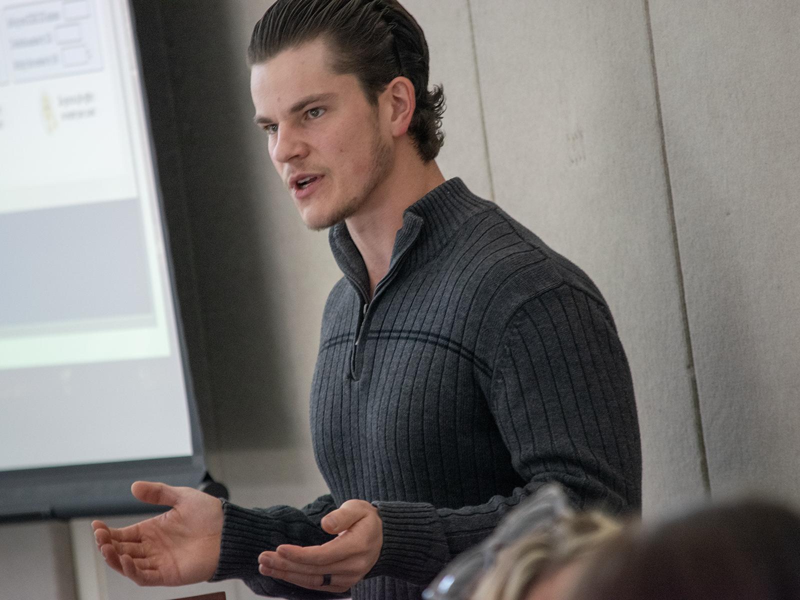 A man speaks in front of a large screen