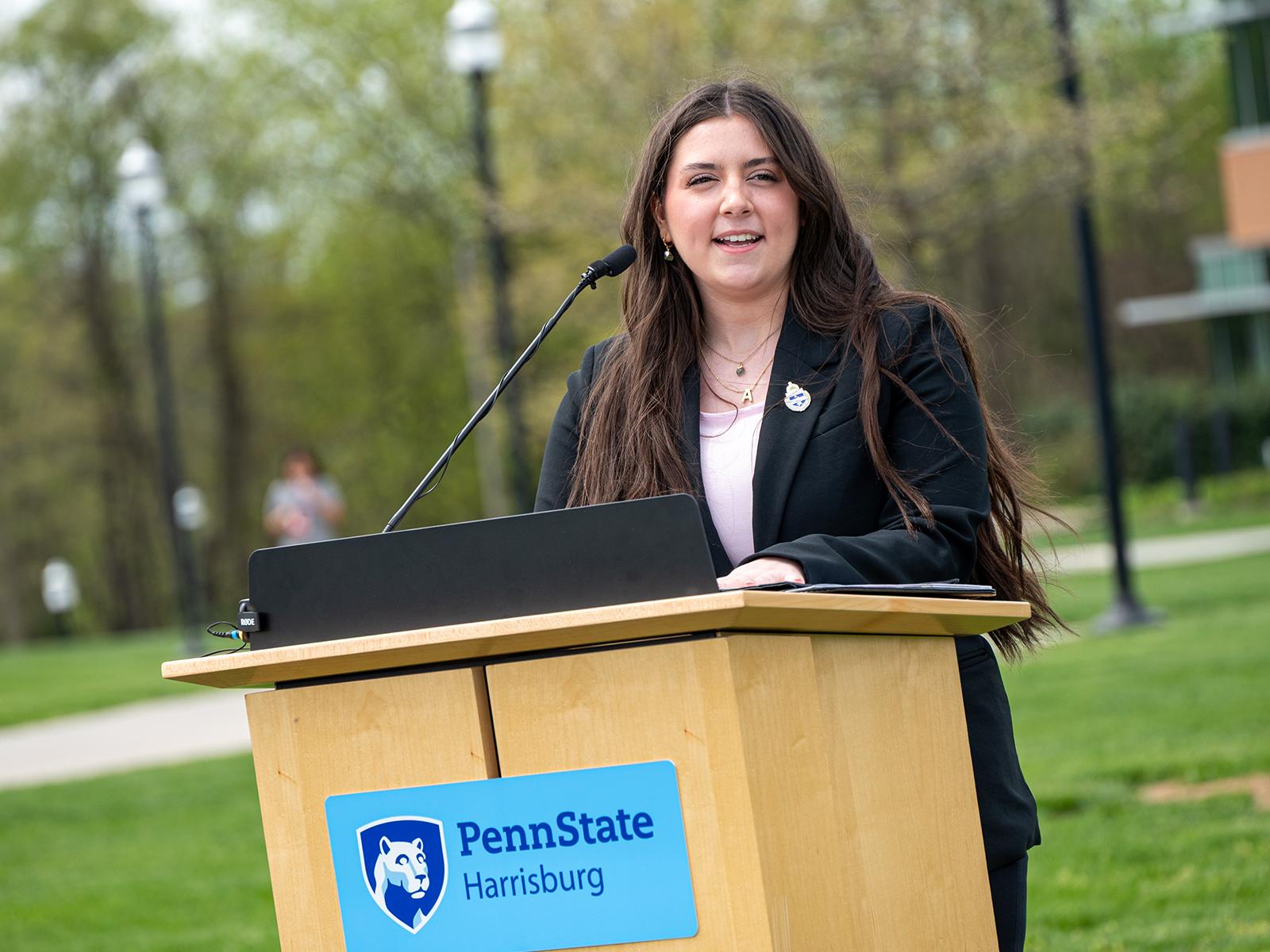 A woman speaks from a lectern outdoors