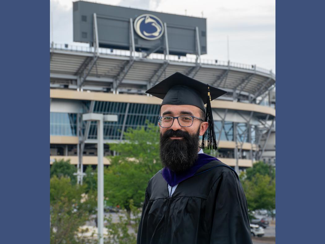 Ali Baghi stands in front of Beaver Stadium in commencement regalia.
