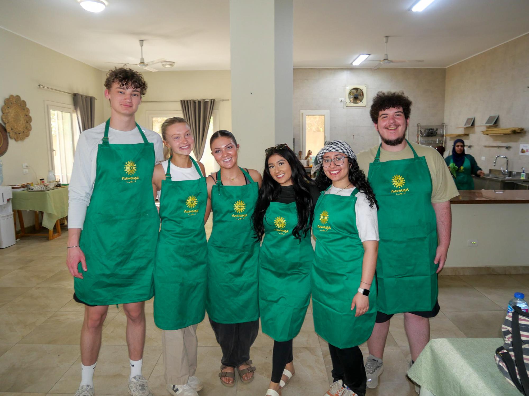 A group of students smiling in green robes in a kitchen for a cooking class in Faiyum, Egypt.