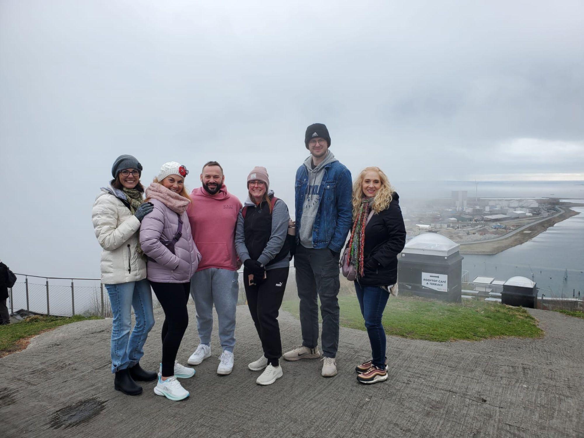 six people stand on a sidewalk overlooking a lower area