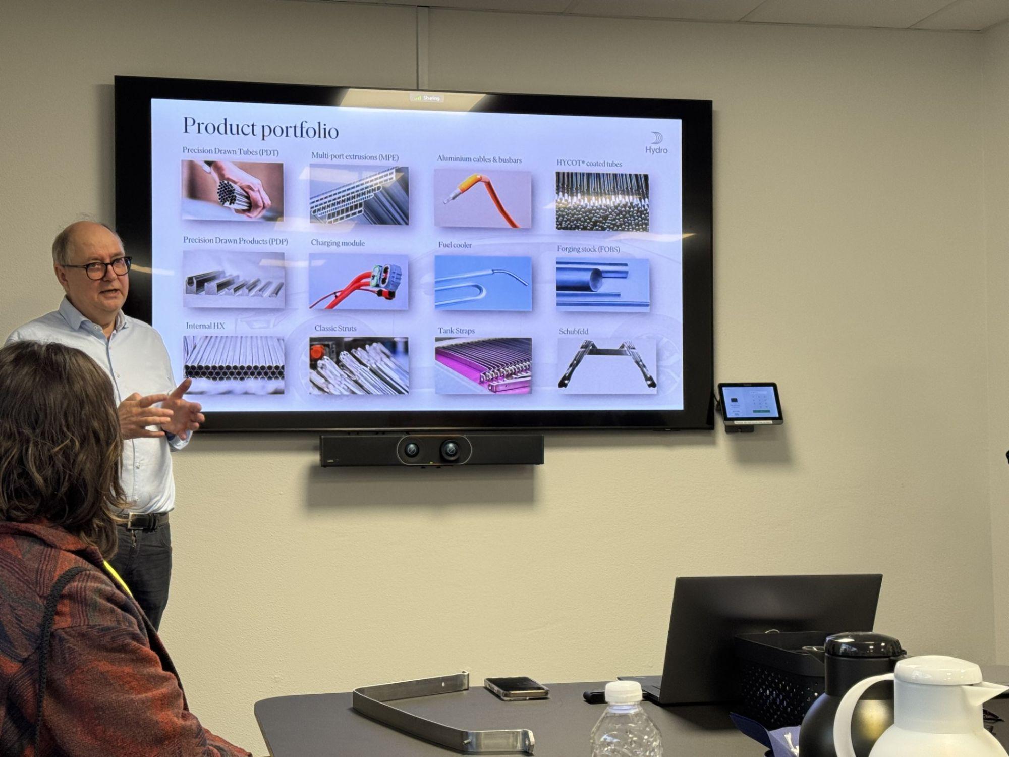 a man stands next to a screen giving a presentation in a conference room while a woman looks on