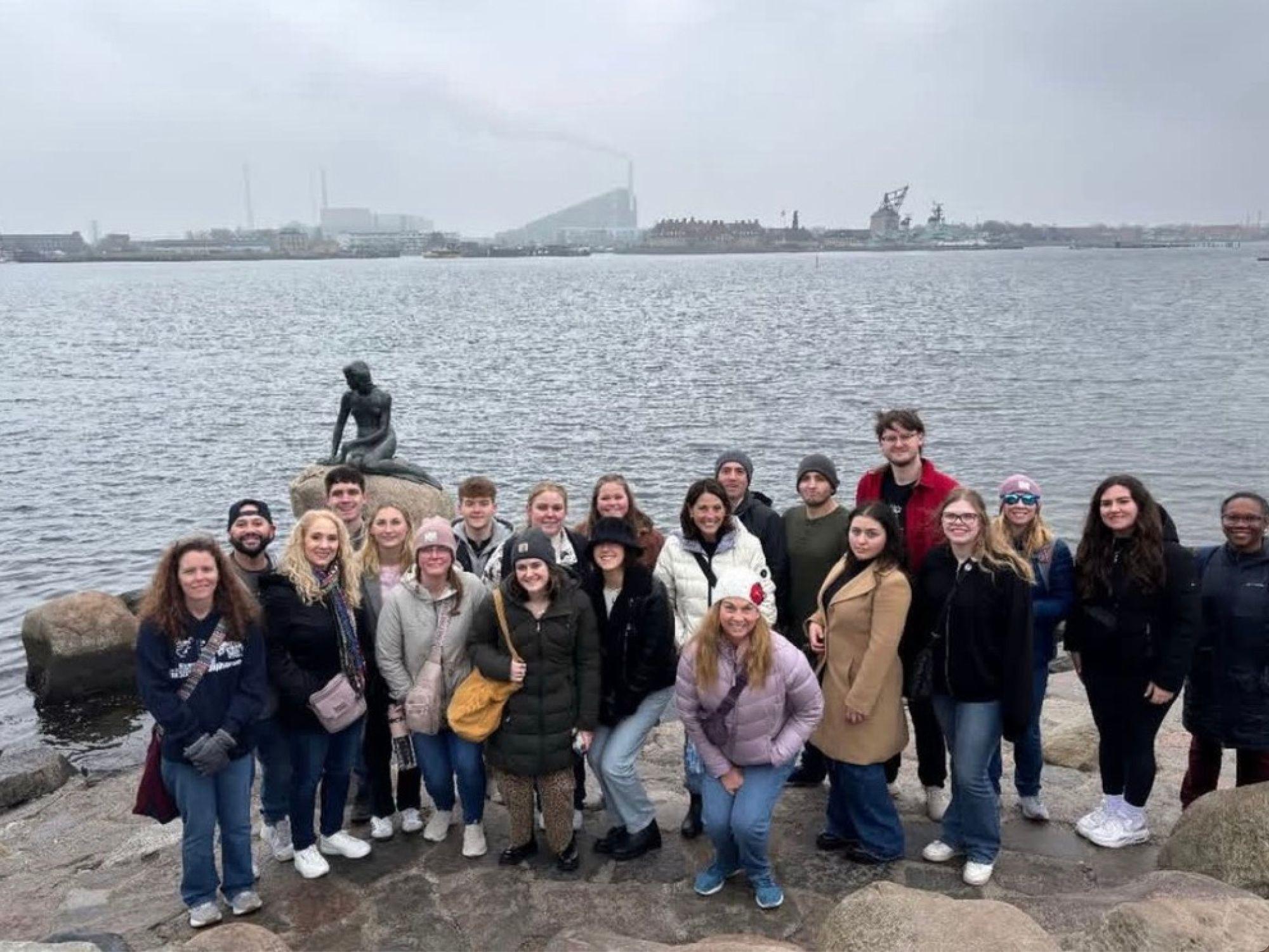 a group of people stand with the little mermaid statue in the background