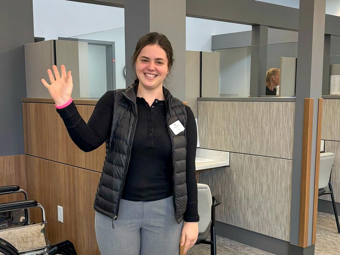 Lucy Taylor waves while standing in the offices of Centre Volunteers in Medicine.