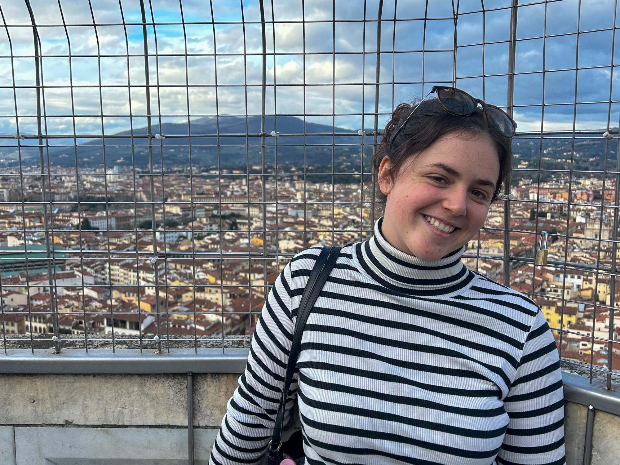 Lucy Taylor stands on the roof of a building overlooking a city in Italy.