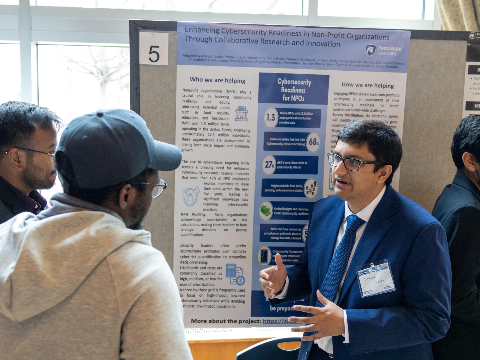 Two master's students explain their nonprofit cybersecurity research project to a visitor