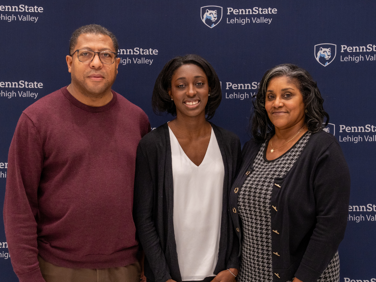 a female student smiles with her parents in front of a Penn State Lehigh Valley backdrop