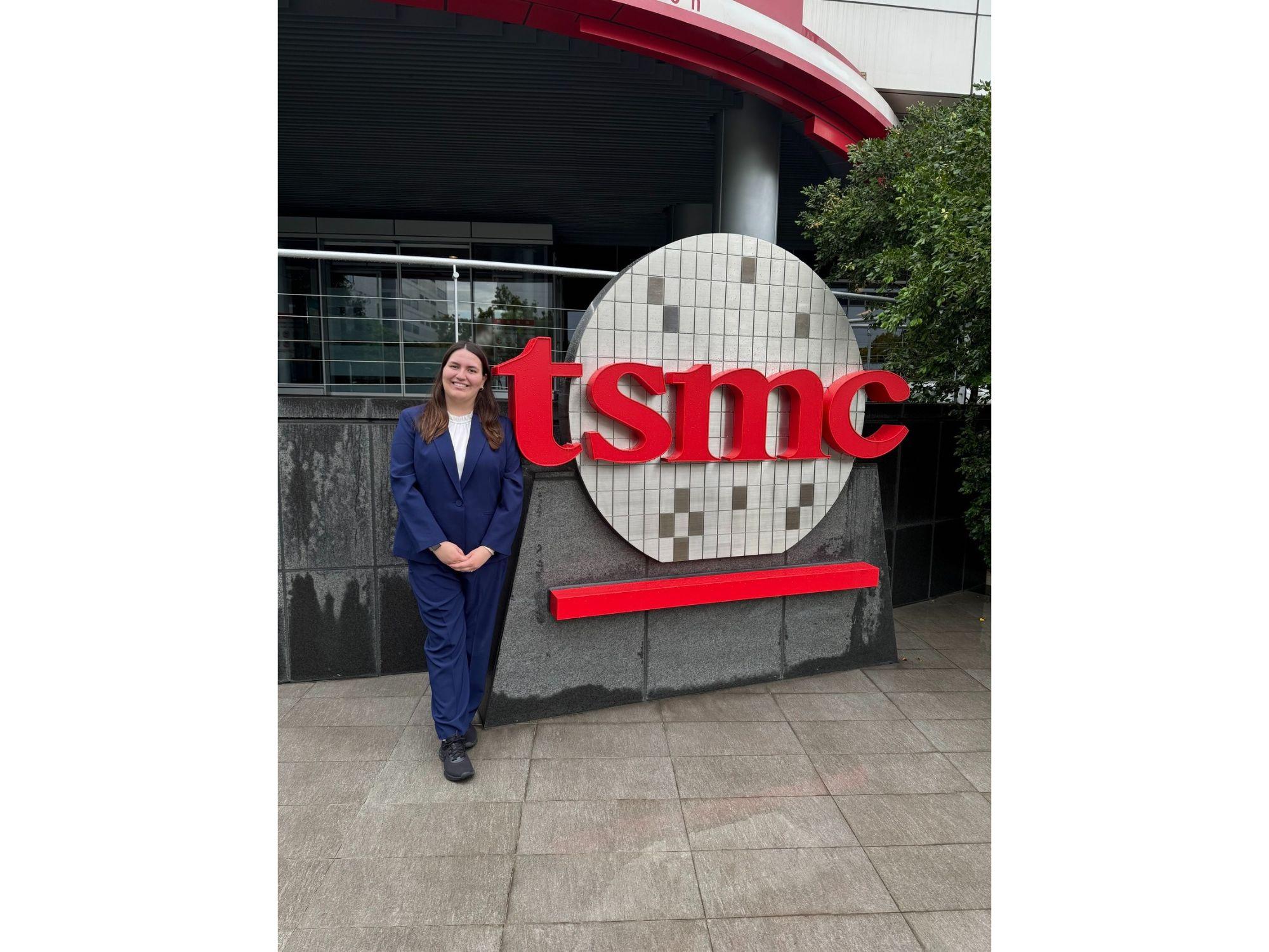 A student stands in front of a company sign that reads "tsmc"
