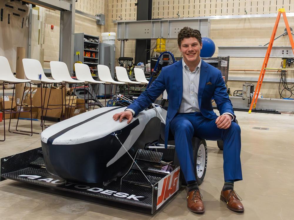 An individual wearing suit leans against a racecar.  