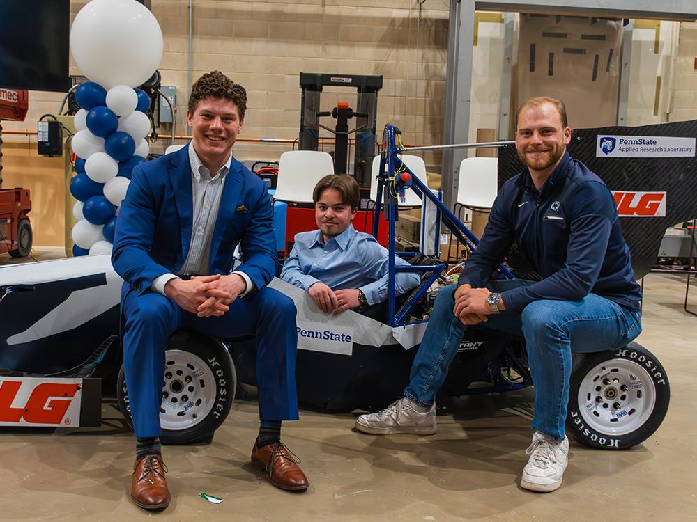 Three individuals pose around a racecar.  