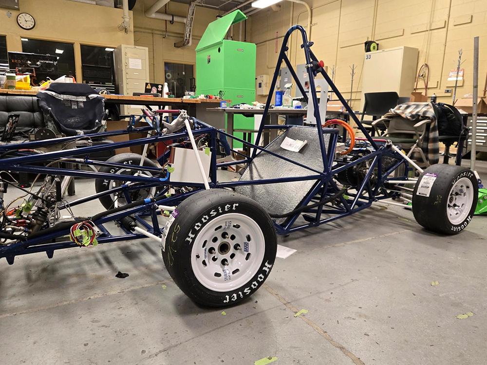 An unfinished racecar is parked inside a garage.