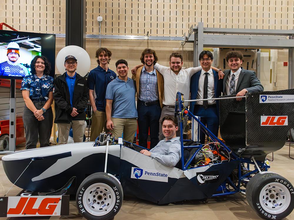 A group of students pose around a racecar.  