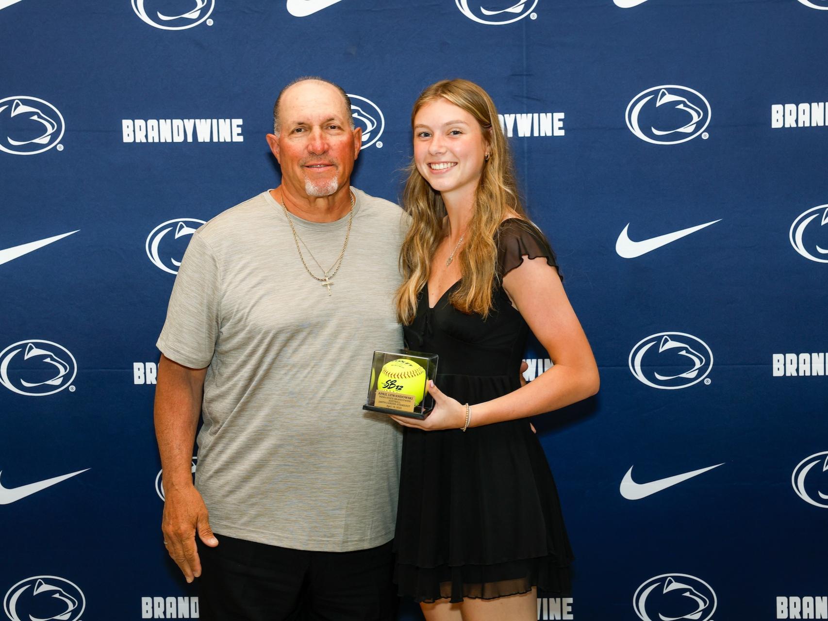 student holding softball with coach