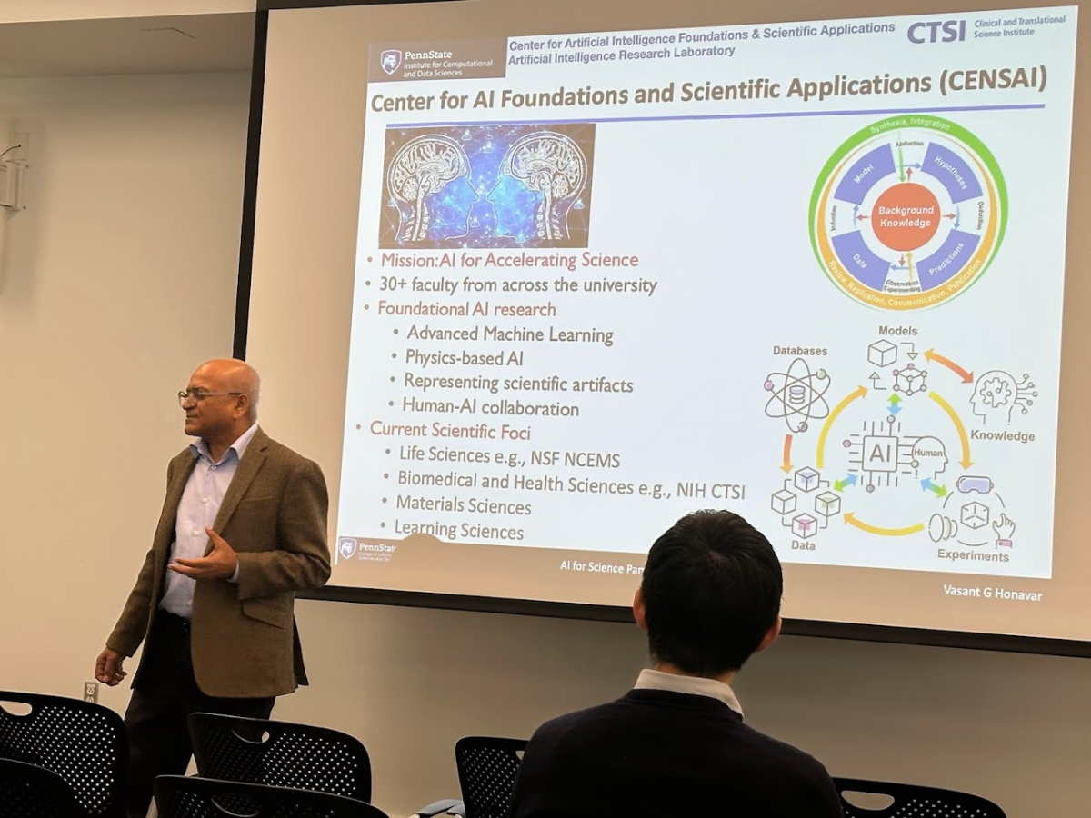 Vasant Honavar, professor in the College of Information Sciences and Technology, stands before a screen presenting his current research focuses during the AI for Science panel.