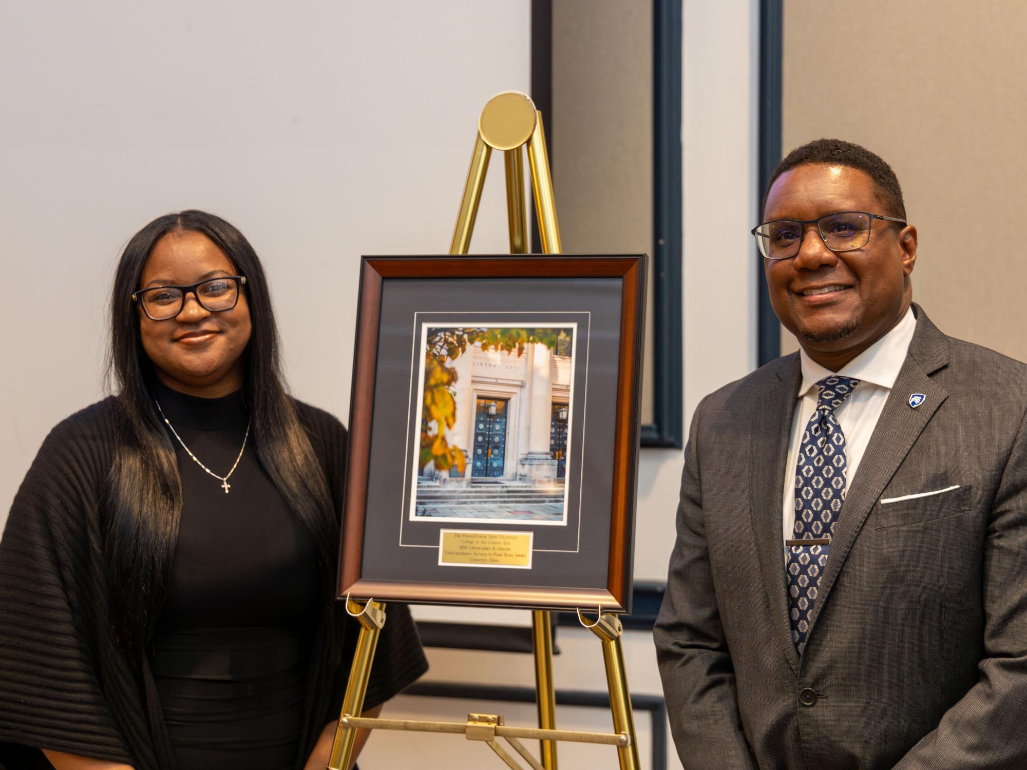 A framed award sits on an easel between Cameryn Allen (left) and Dean Clarence Lang (right).