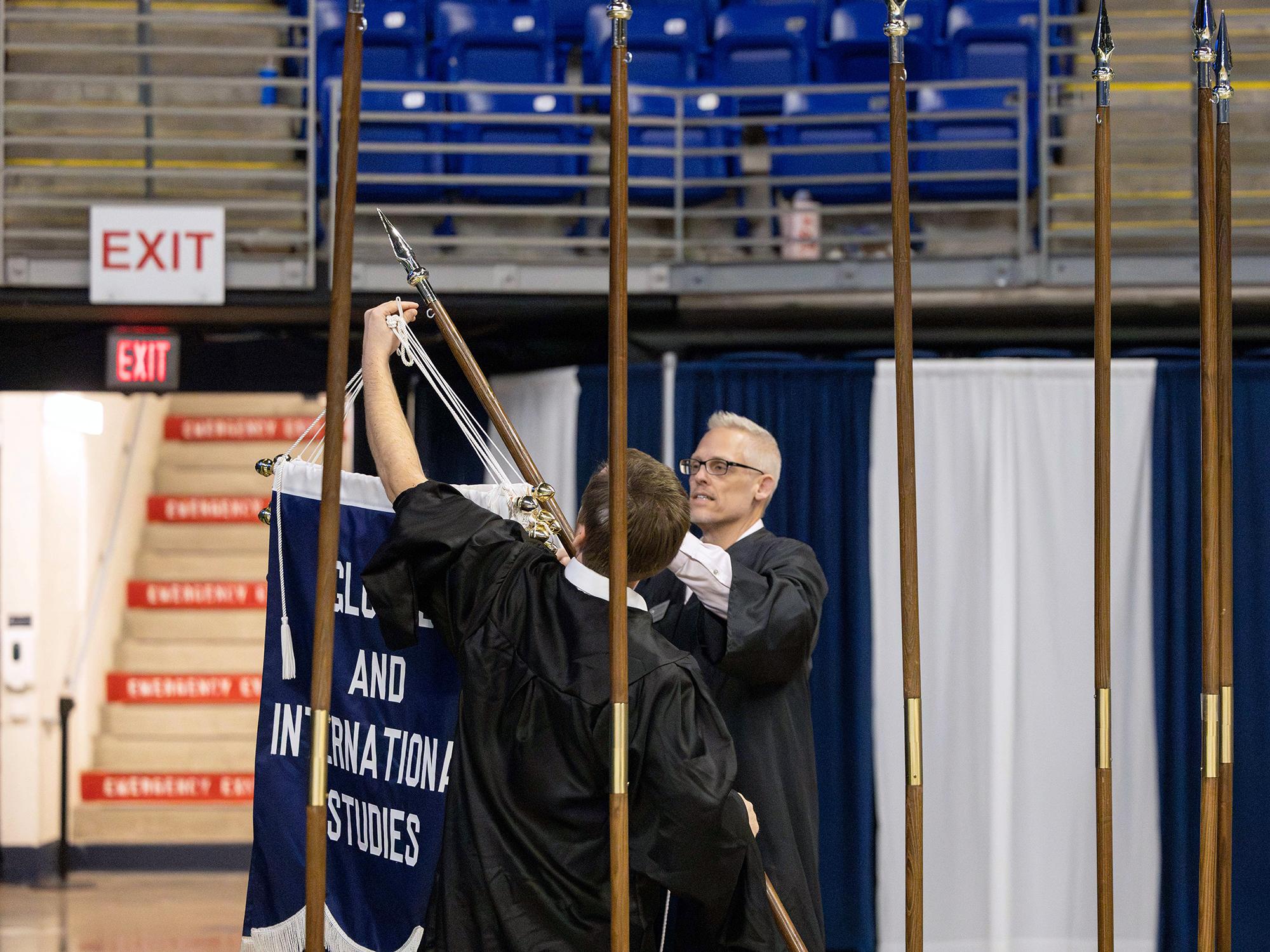Two people hang a banner on a pole at the front of an event space