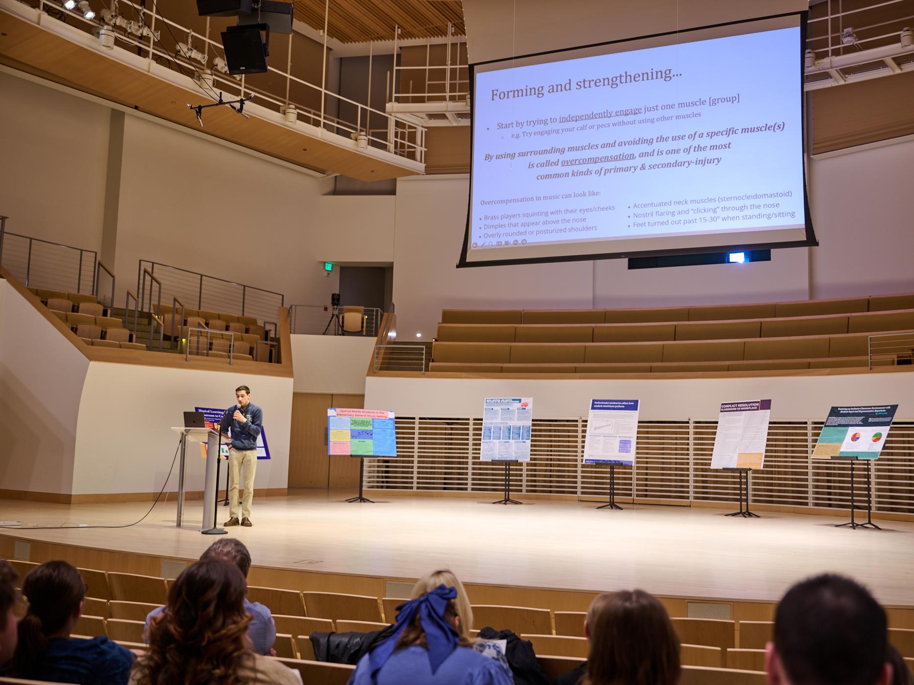 Student presenting slideshow on stage at Recital Hall