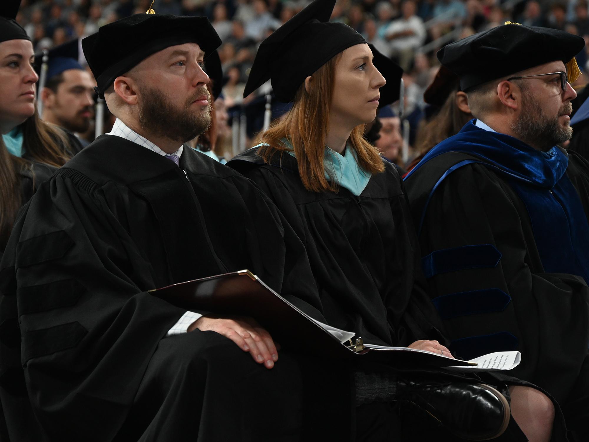 Two people sit together during commencement ceremonies, facing the stage