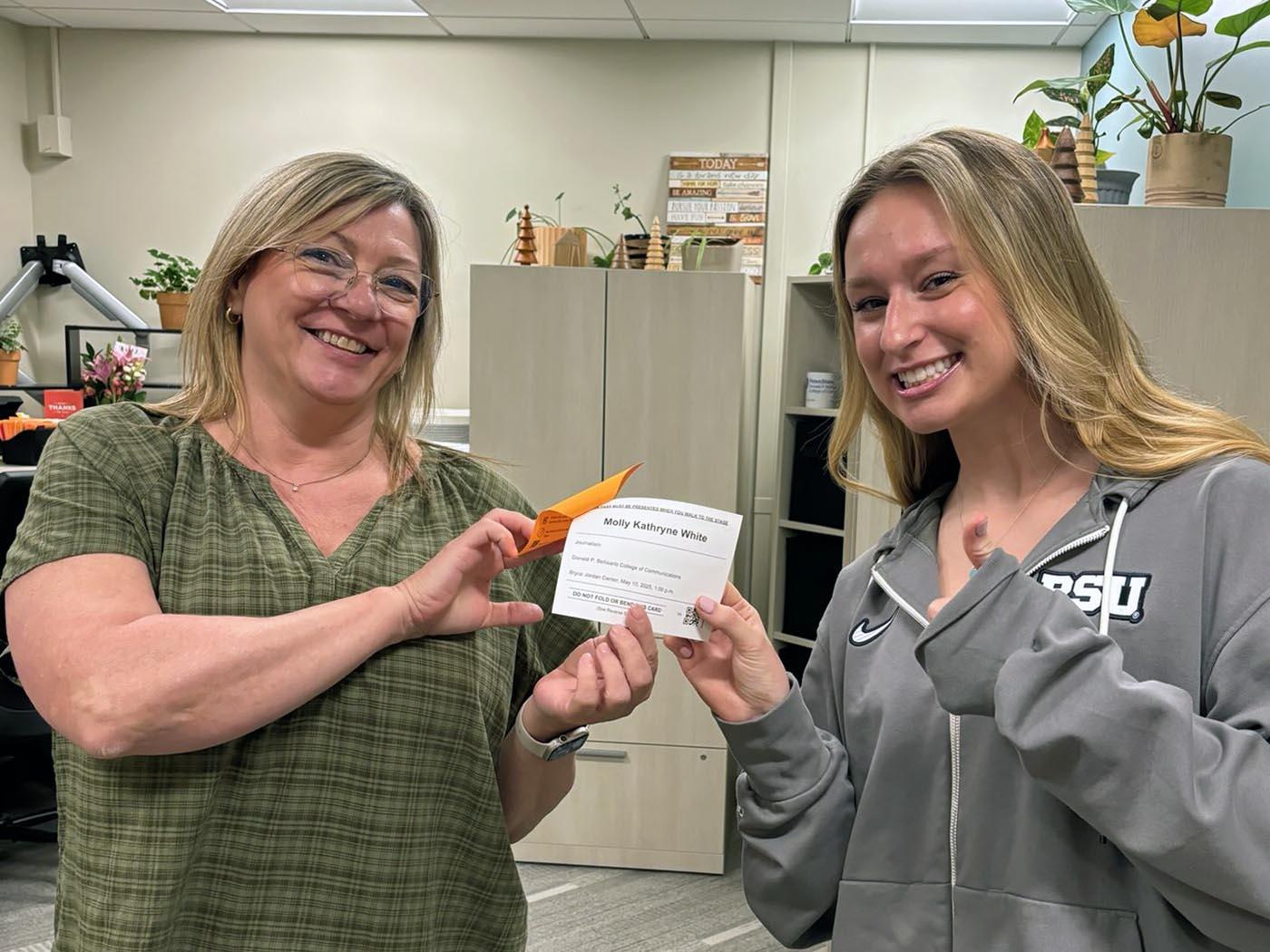 A woman holds a card with a student, each posing and smiling for the camera.