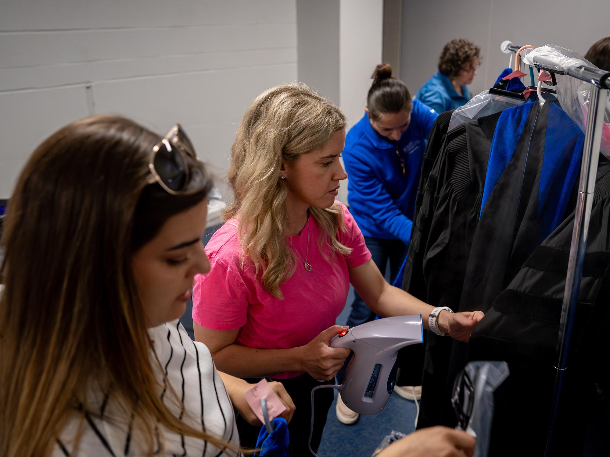 Three women stand in a line and steam commencement gowns