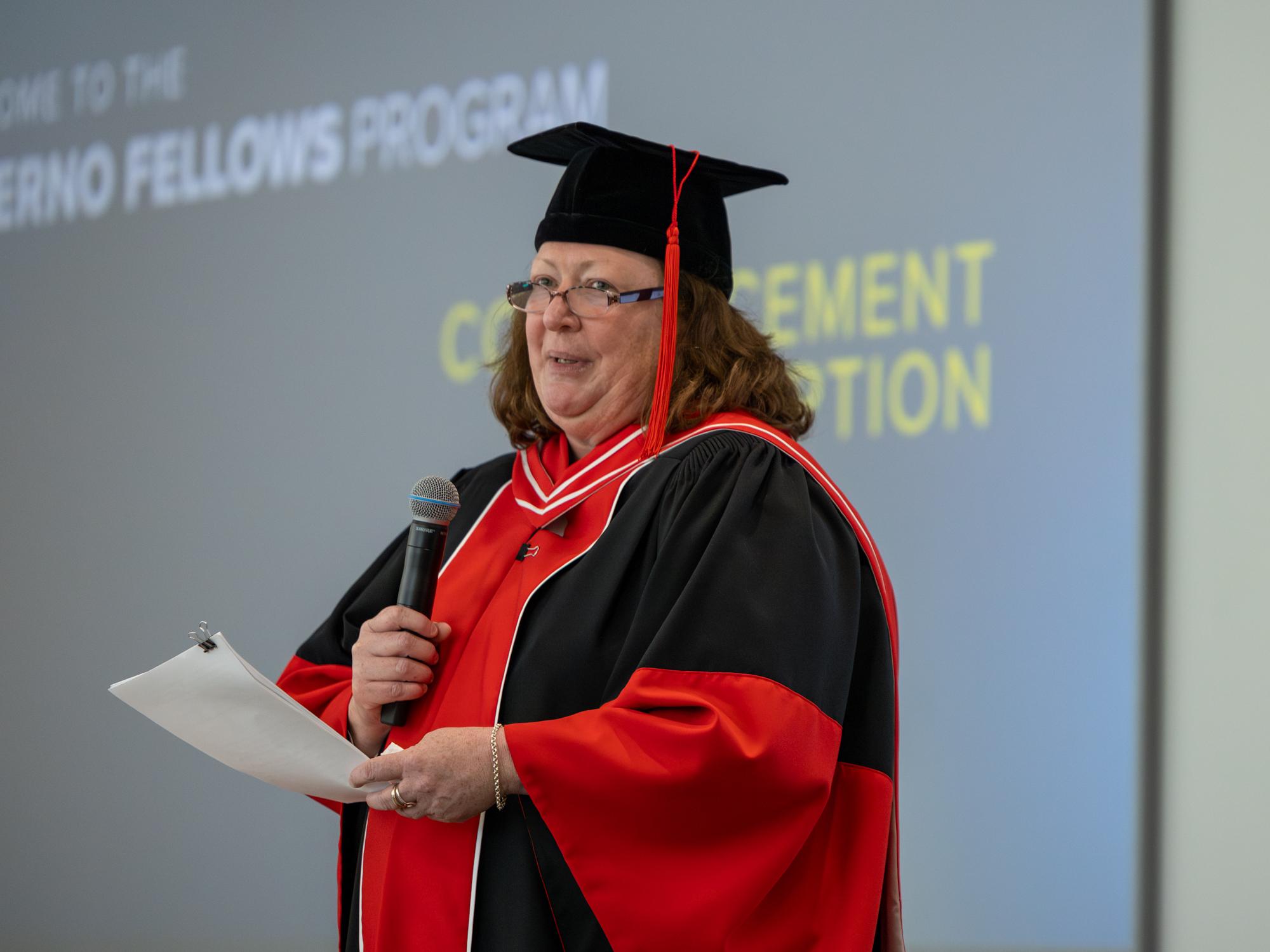 Photo of Kathyrn Salzer holding a mic and wearing doctoral regalia. 