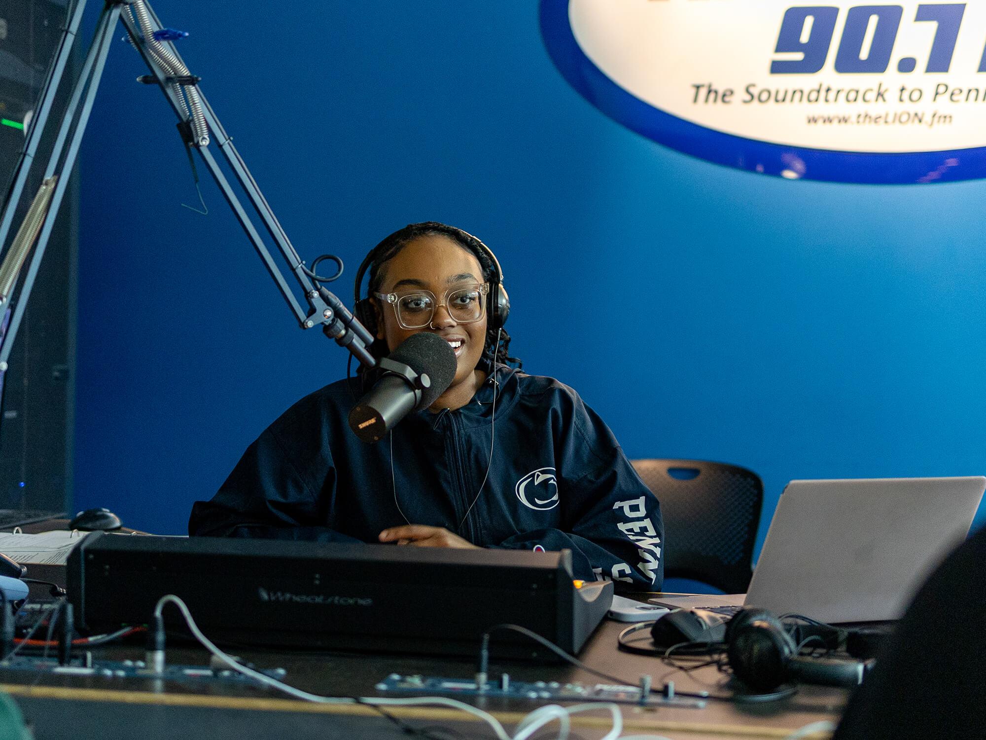 Kyla Pritchett sits behind a microphone and an audio control board in The Lion 90.7fm studio
