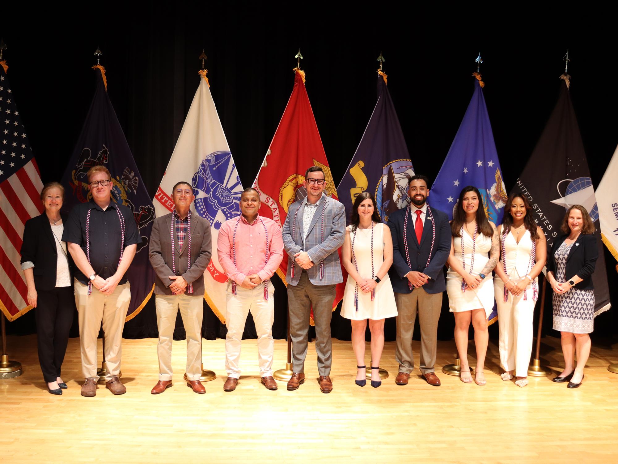 A group of people pose in front of the American flag and U.S. military flags.