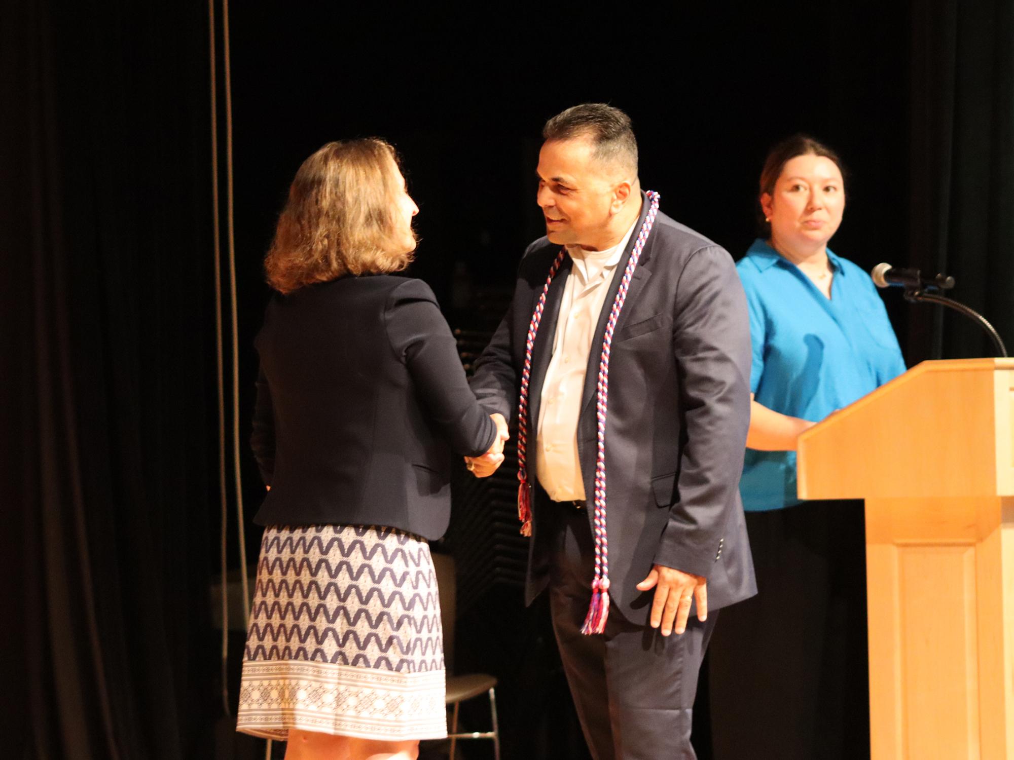 A man shakes a woman's hand on a stage.