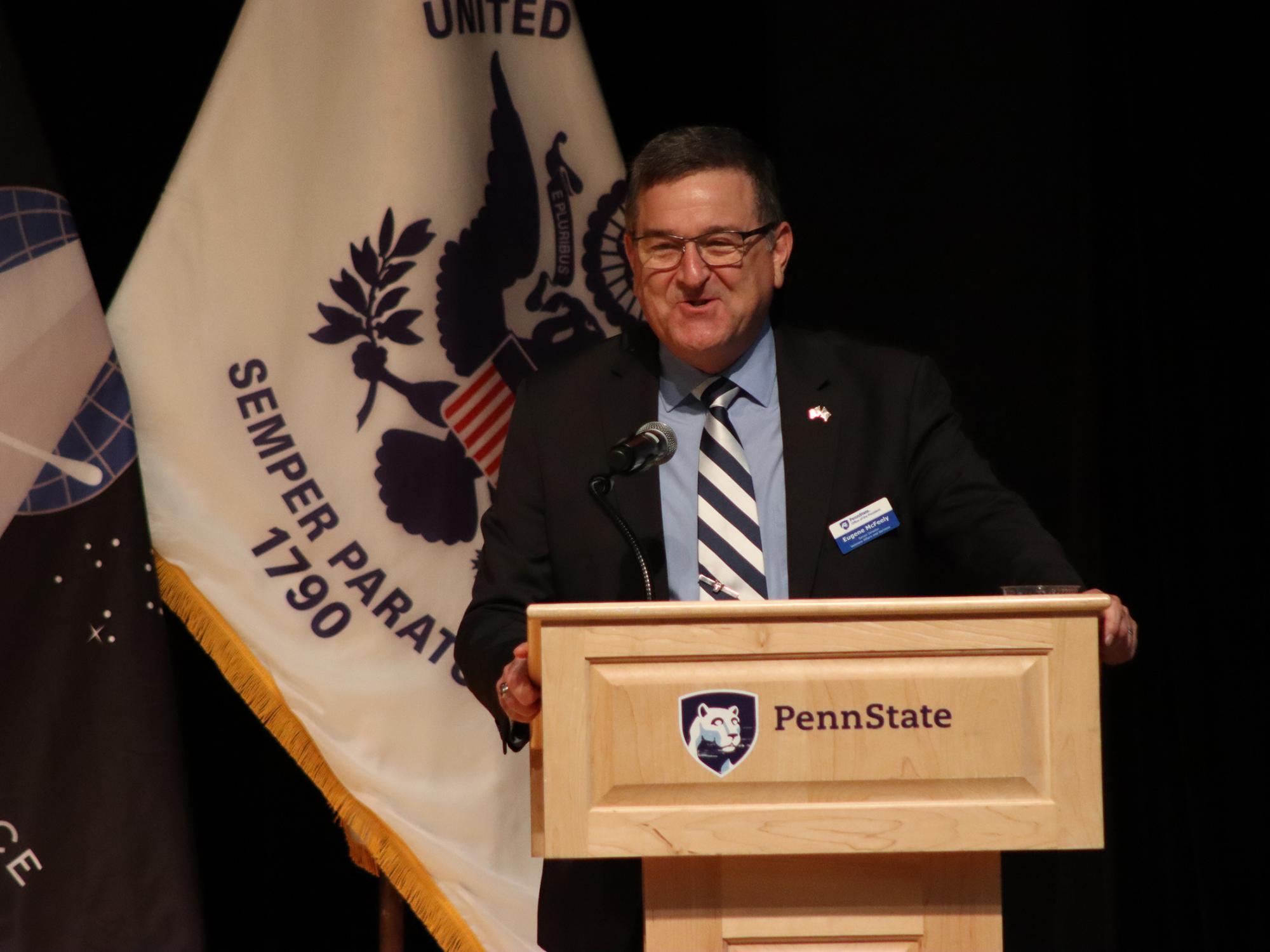 A man speaks at a podium in front of a group of flags.