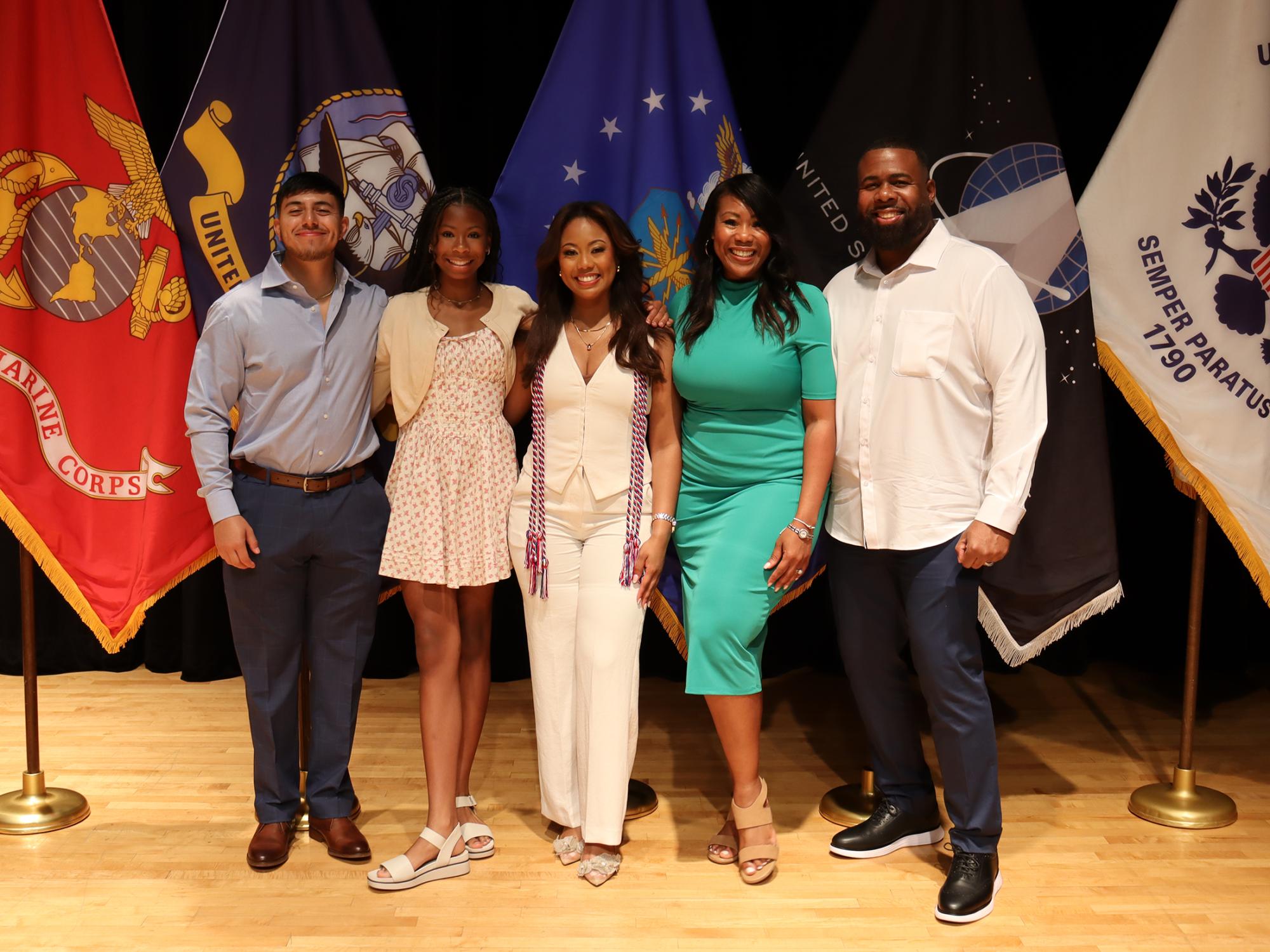 Five people pose in front of U.S. military flags.
